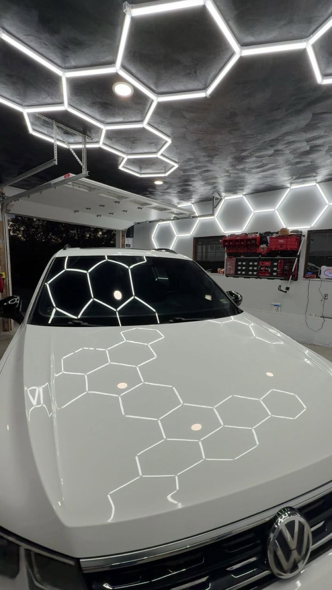 Glossy white Volkswagen reflecting hexagon shop lights after detailing